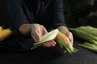 Woman husking corn cob at black table, closeup