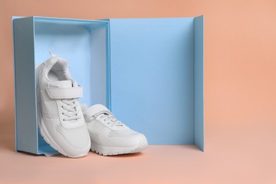 Photo of Pair of comfortable sports shoes and box on pale coral background. Space for text