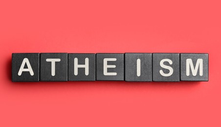 Word Atheism made of black wooden cubes with letters on red textured table, top view
