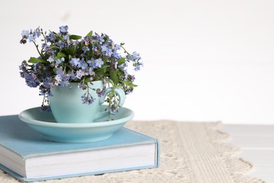 Photo of Beautiful forget-me-not flowers in cup, saucer and book on table against white background, closeup. Space for text
