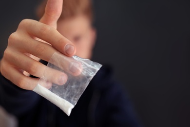 Photo of Criminal holding plastic bag with drug against dark background, space for text