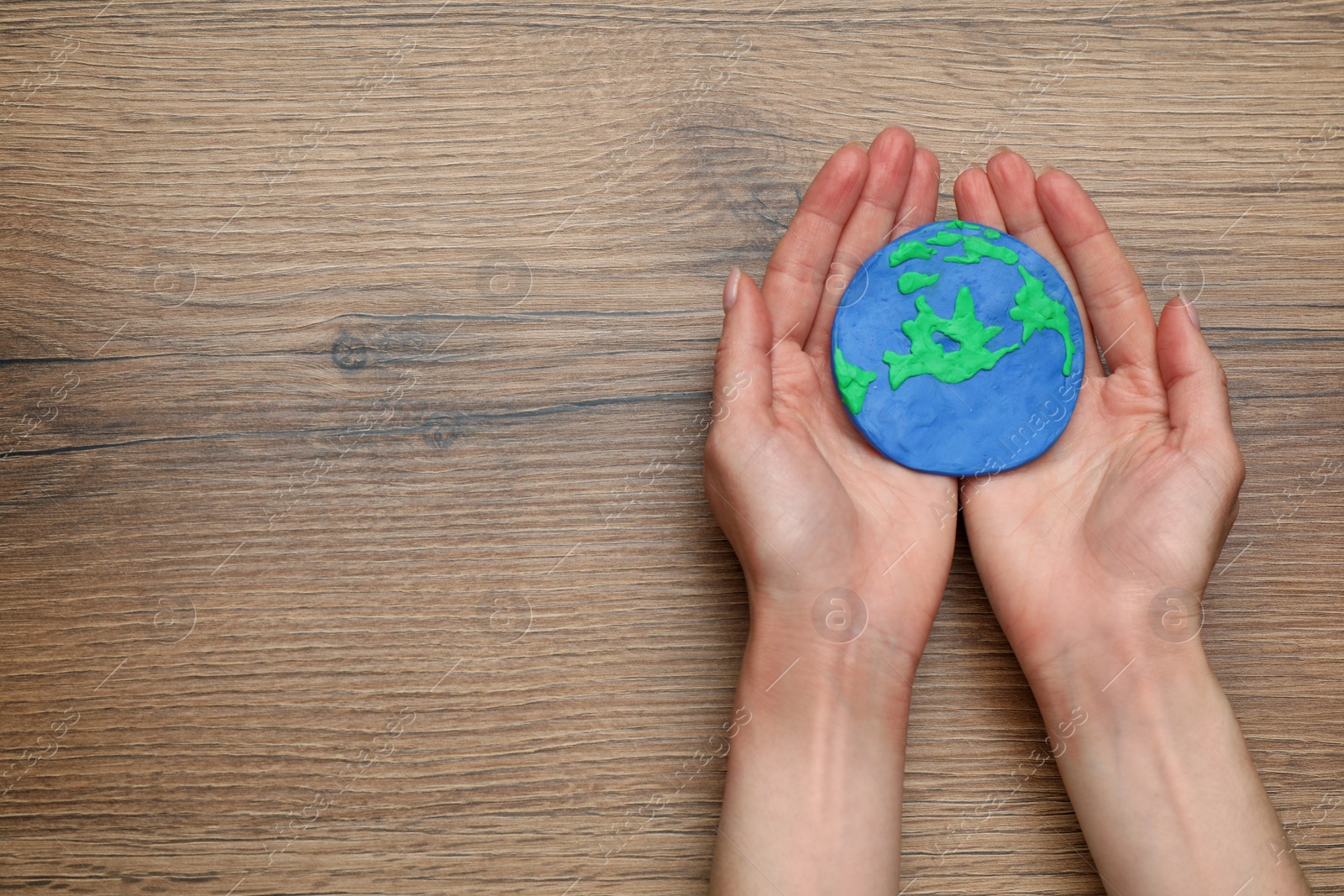 Photo of Happy Earth Day. Woman with plasticine planet at wooden table, top view and space for text