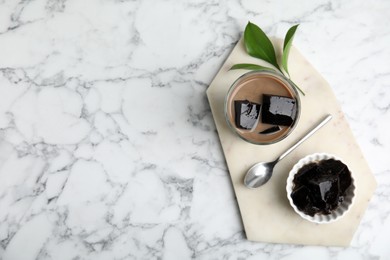 Photo of Glass of milk with grass jelly on white marble table, top view. Space for text