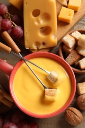 Photo of Pot of tasty cheese fondue and snacks on wooden table, flat lay