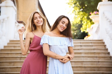 Photo of Beautiful young women in stylish dresses on stairs outdoors