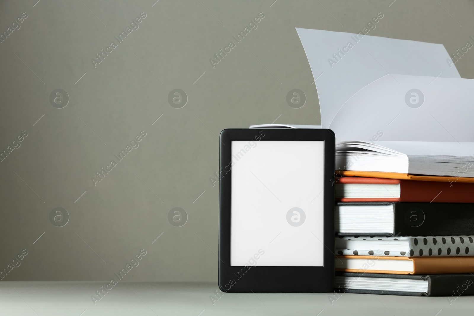 Photo of Modern e-book reader and stack of hard cover books on light grey table. Space for text