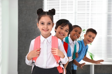 Photo of Happy children in school uniform with backpacks indoors