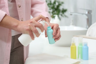 Photo of Woman pouring cosmetic product into plastic bottle over white countertop in bathroom, closeup and space for text. Bath accessories