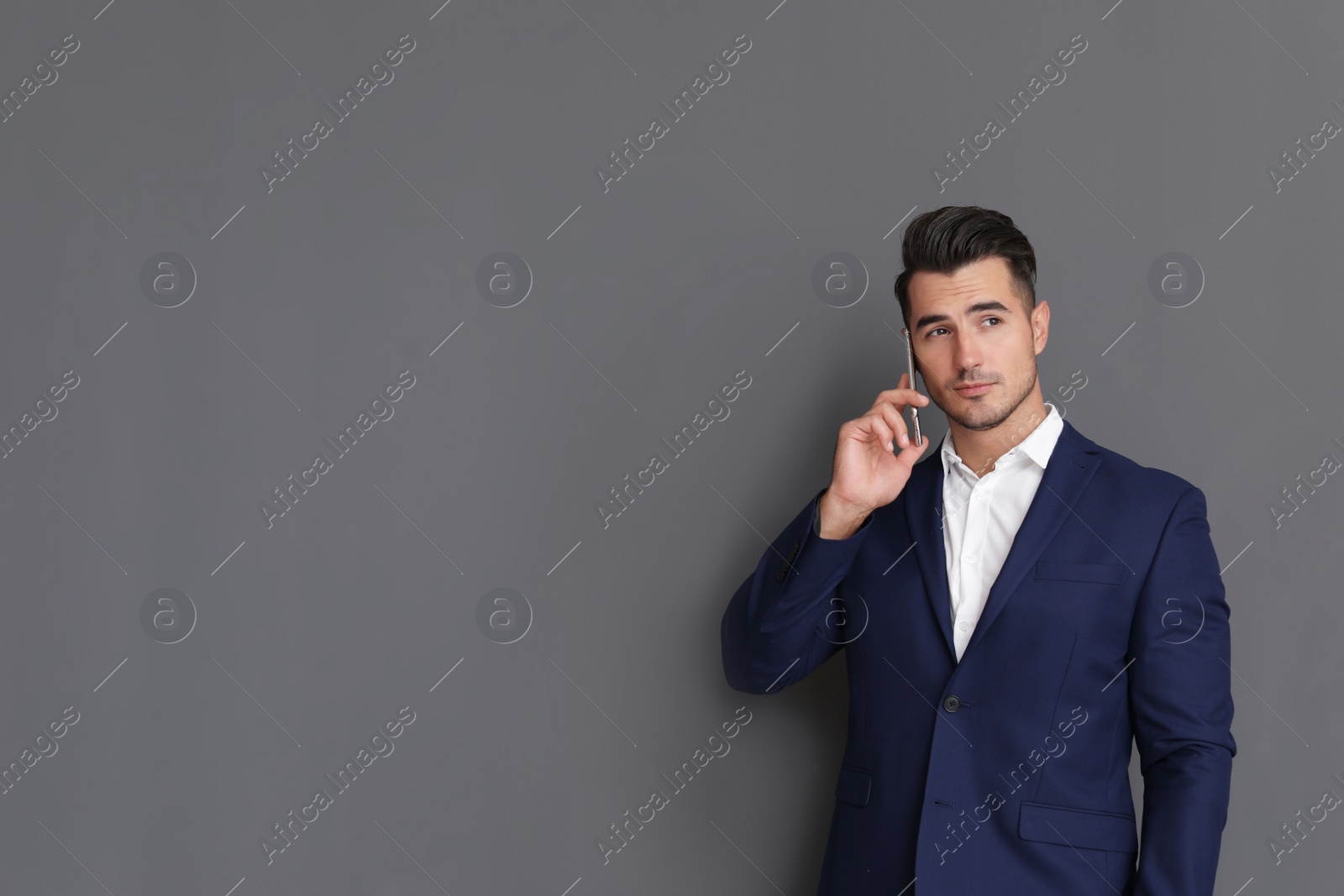 Photo of Handsome young man talking on phone against grey background. Space for text