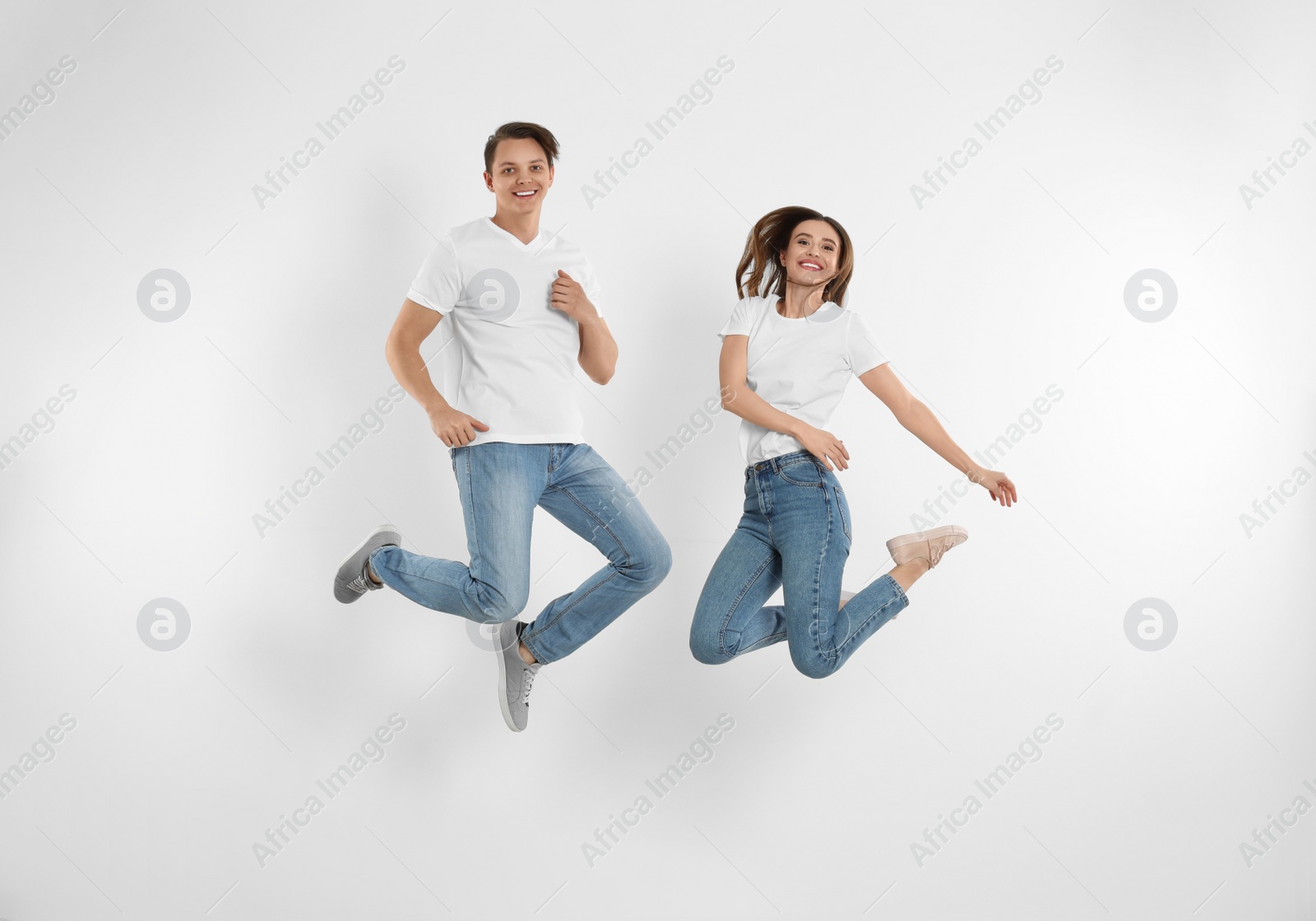 Photo of Young couple in stylish jeans jumping near white wall
