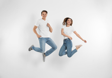 Young couple in stylish jeans jumping near white wall