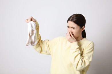 Young woman feeling bad smell from dirty socks on light grey background