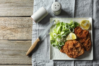 Tasty schnitzels served with lemon and salad on wooden table, flat lay. Space for text