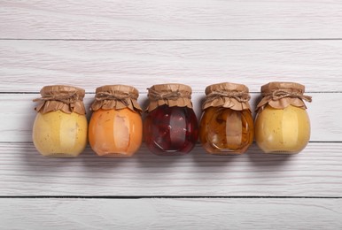 Jars with preserved fruit jams on white wooden table, flat lay