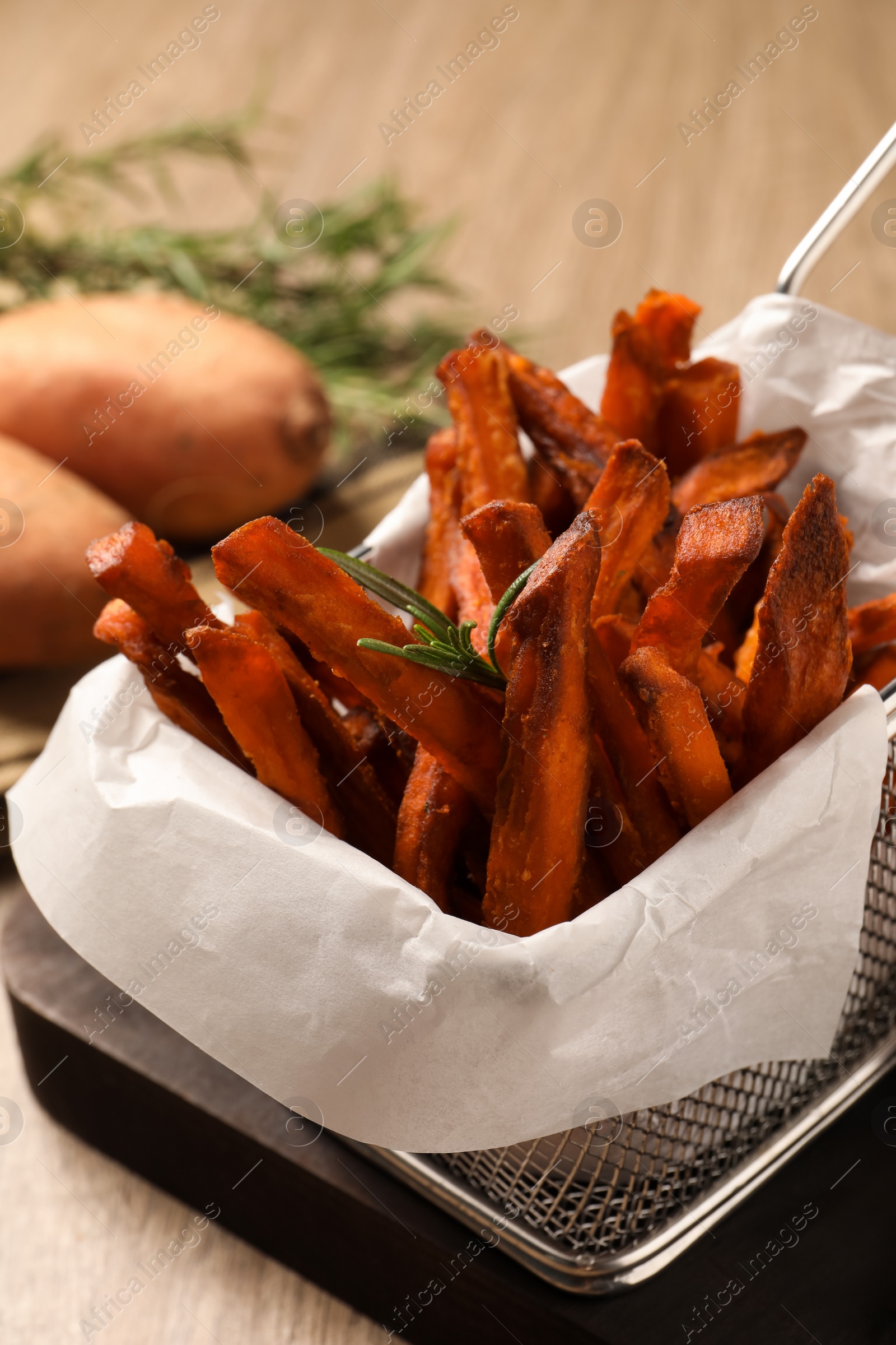 Photo of Frying basket with sweet potato fries on table, closeup