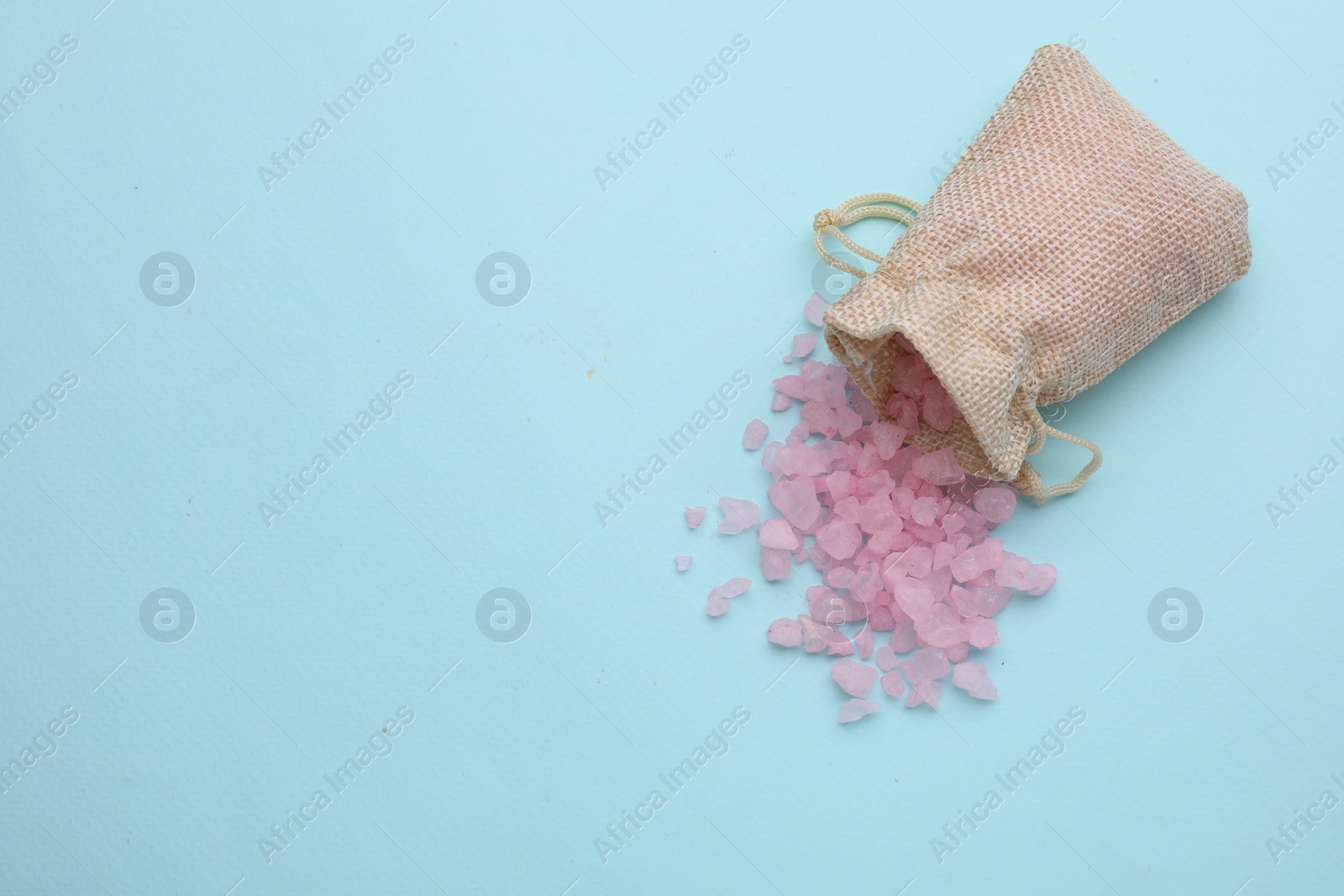 Photo of Bag with pink sea salt on light blue background, top view. Space for text