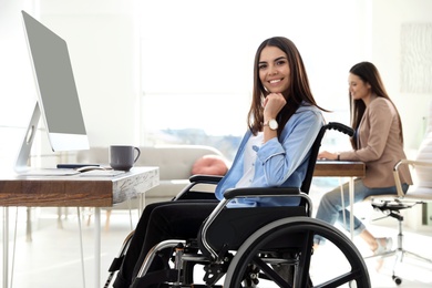 Photo of Young woman in wheelchair using computer at workplace