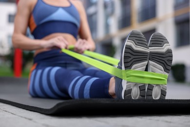 Woman doing exercise with fitness elastic band on mat outdoors, closeup