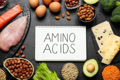 Photo of Different fresh products and notebook with words Amino Acids on black table, flat lay