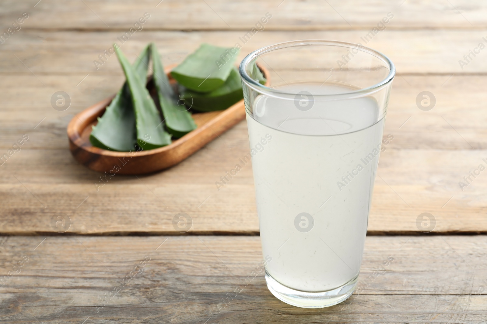 Photo of Tasty aloe juice in glass and cut fresh leaves on wooden table, closeup