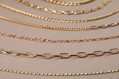 Photo of Different metal chains on light brown background, closeup. Luxury jewelry