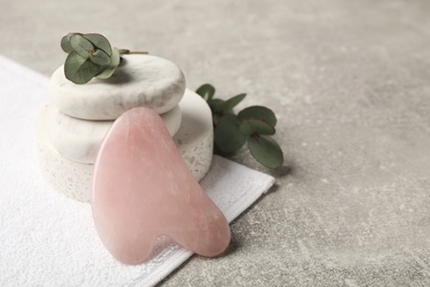Photo of Rose quartz gua sha tool, spa stones and eucalyptus branches on grey table, space for text