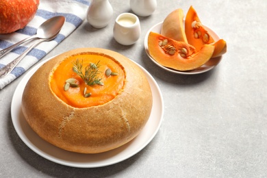 Photo of Tasty pumpkin soup served in bread on gray table