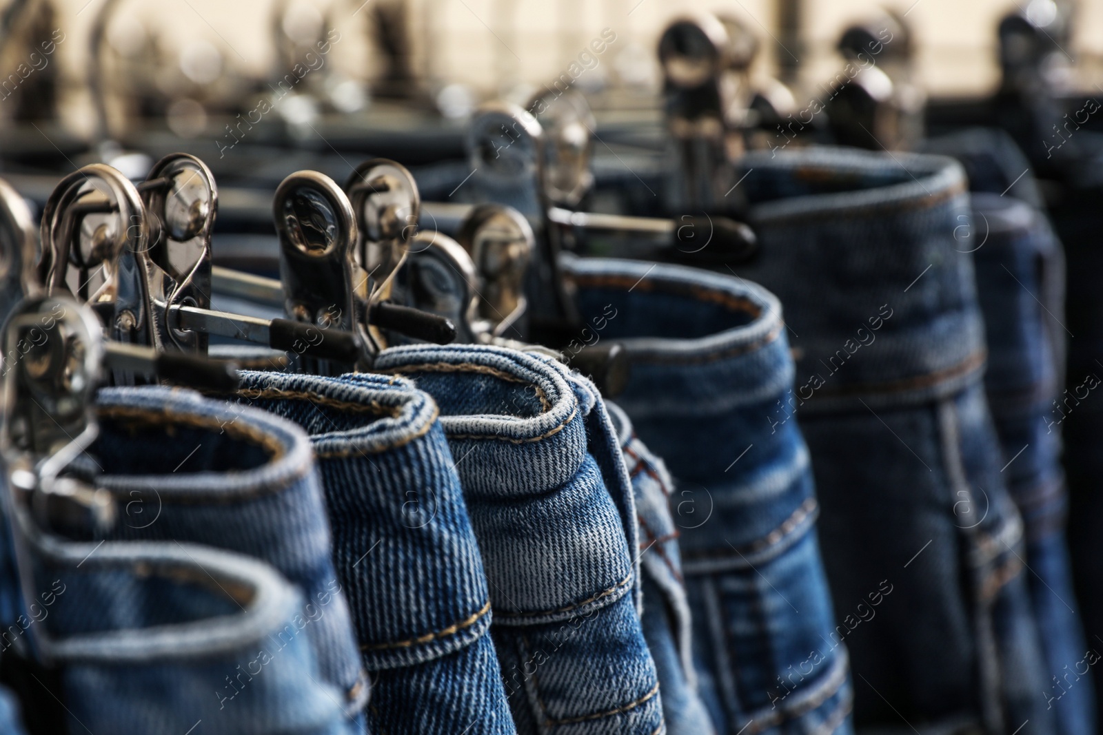 Photo of Different stylish jeans on metal hangers, closeup