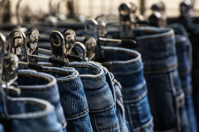 Different stylish jeans on metal hangers, closeup