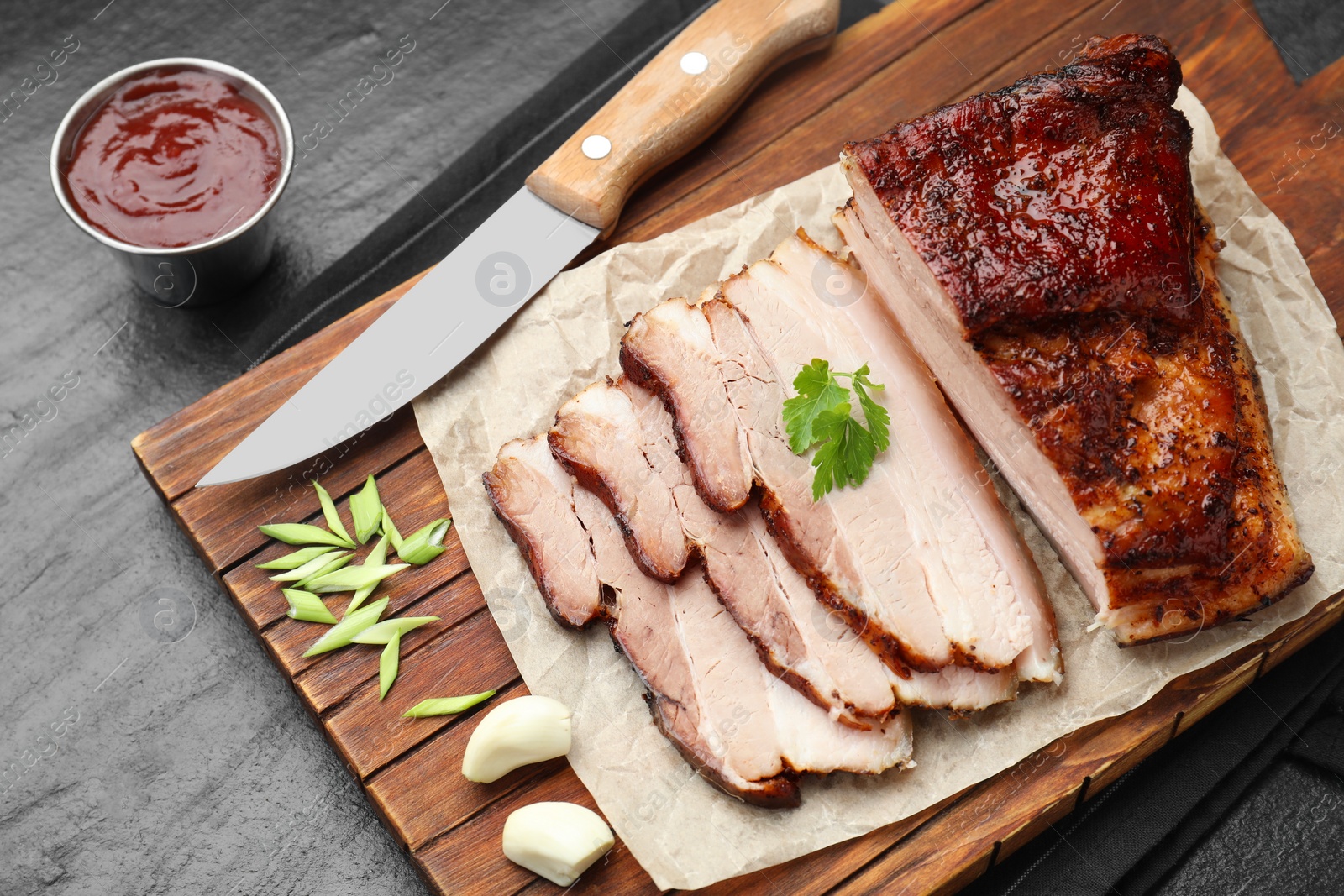 Photo of Pieces of baked pork belly served with sauce and parsley on black textured table, above view