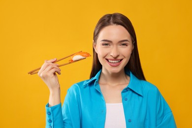 Happy beautiful young woman holding sushi with chopsticks on orange background