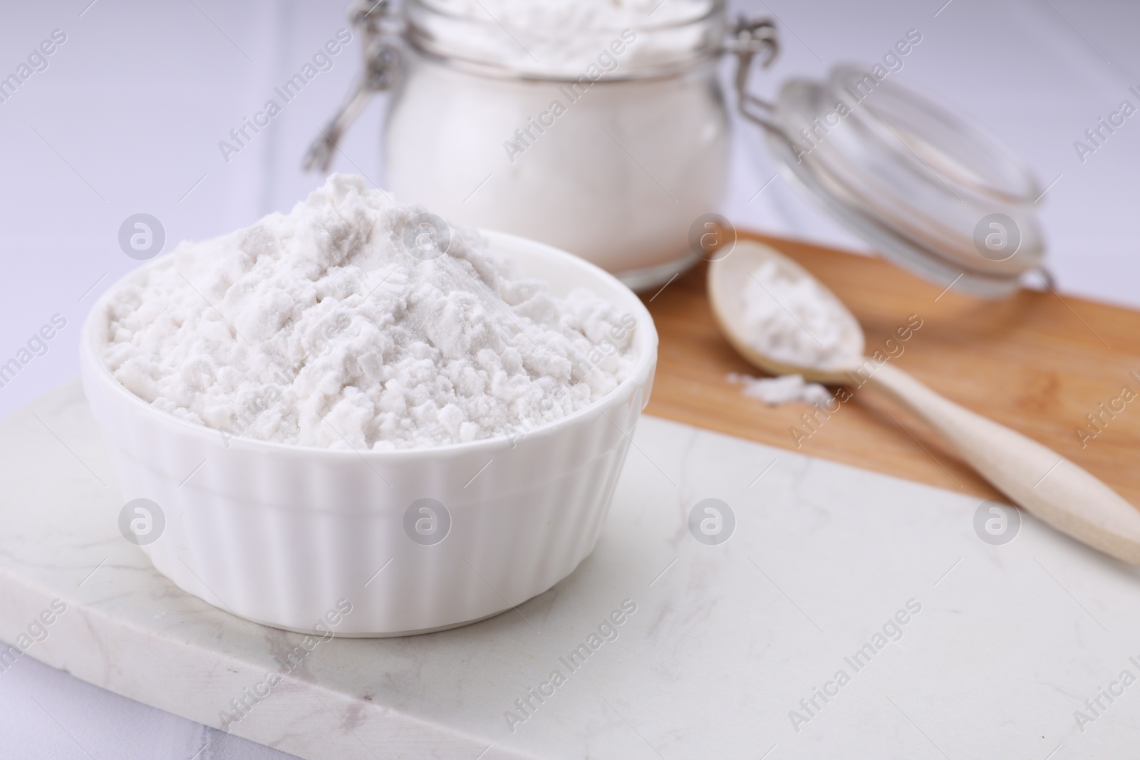 Photo of Bowl and spoon of natural starch on white table, closeup. Space for text