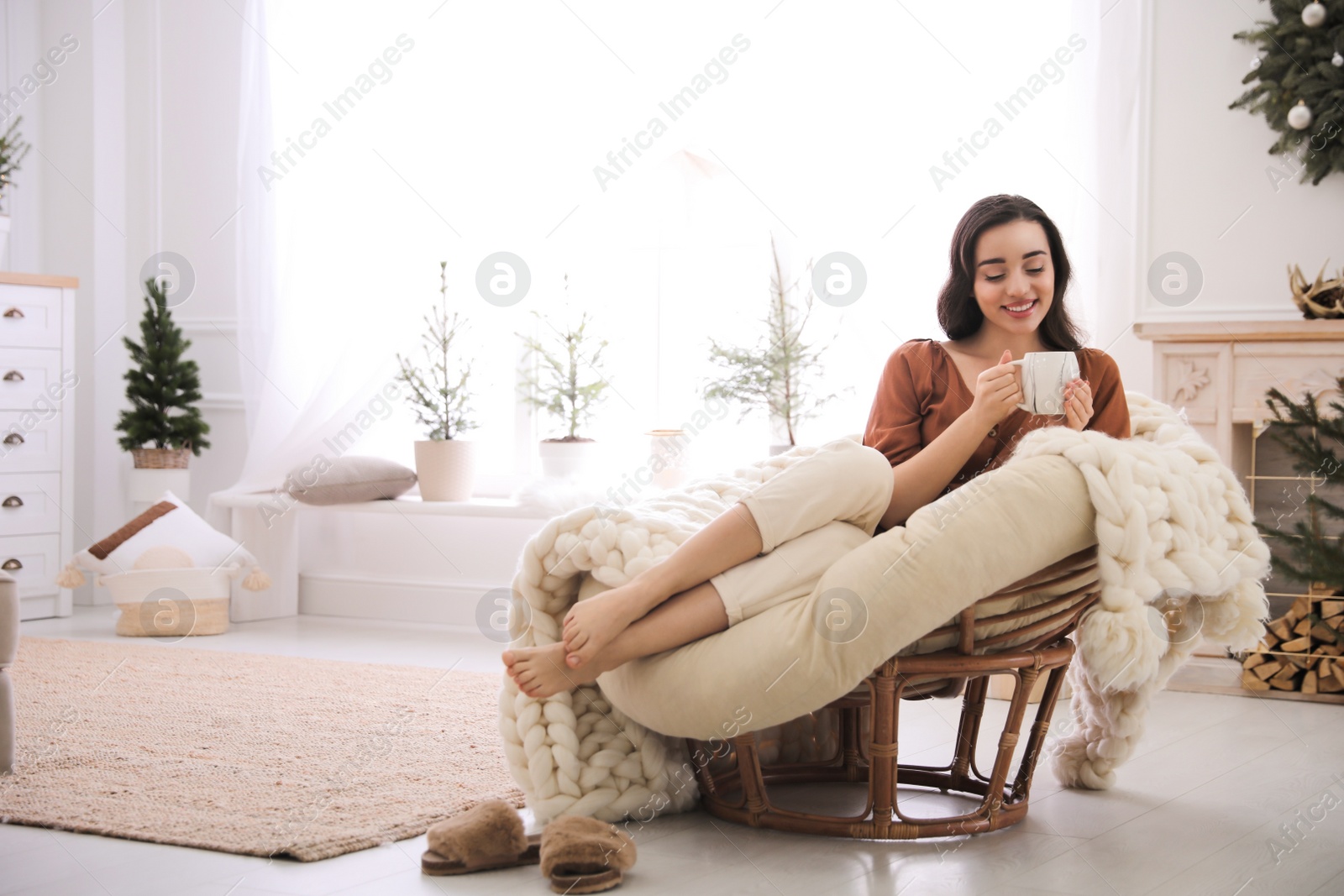 Photo of Woman with hot drink resting in comfortable papasan chair at home. Space for text