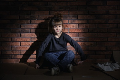 Poor little girl sitting on floor near brick wall
