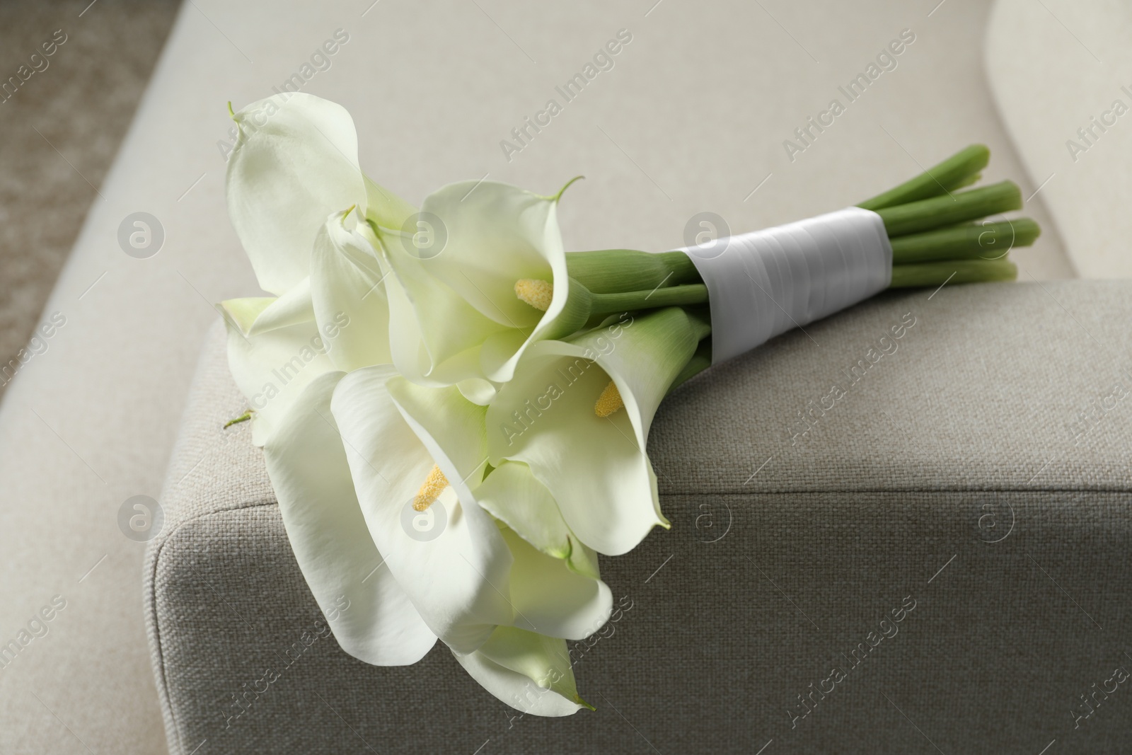 Photo of Beautiful calla lily flowers tied with ribbon on sofa indoors