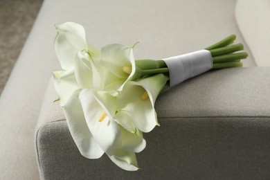 Beautiful calla lily flowers tied with ribbon on sofa indoors