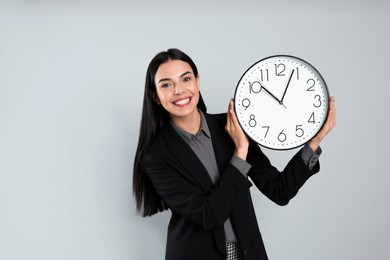 Photo of Businesswoman holding clock on light grey background. Time management
