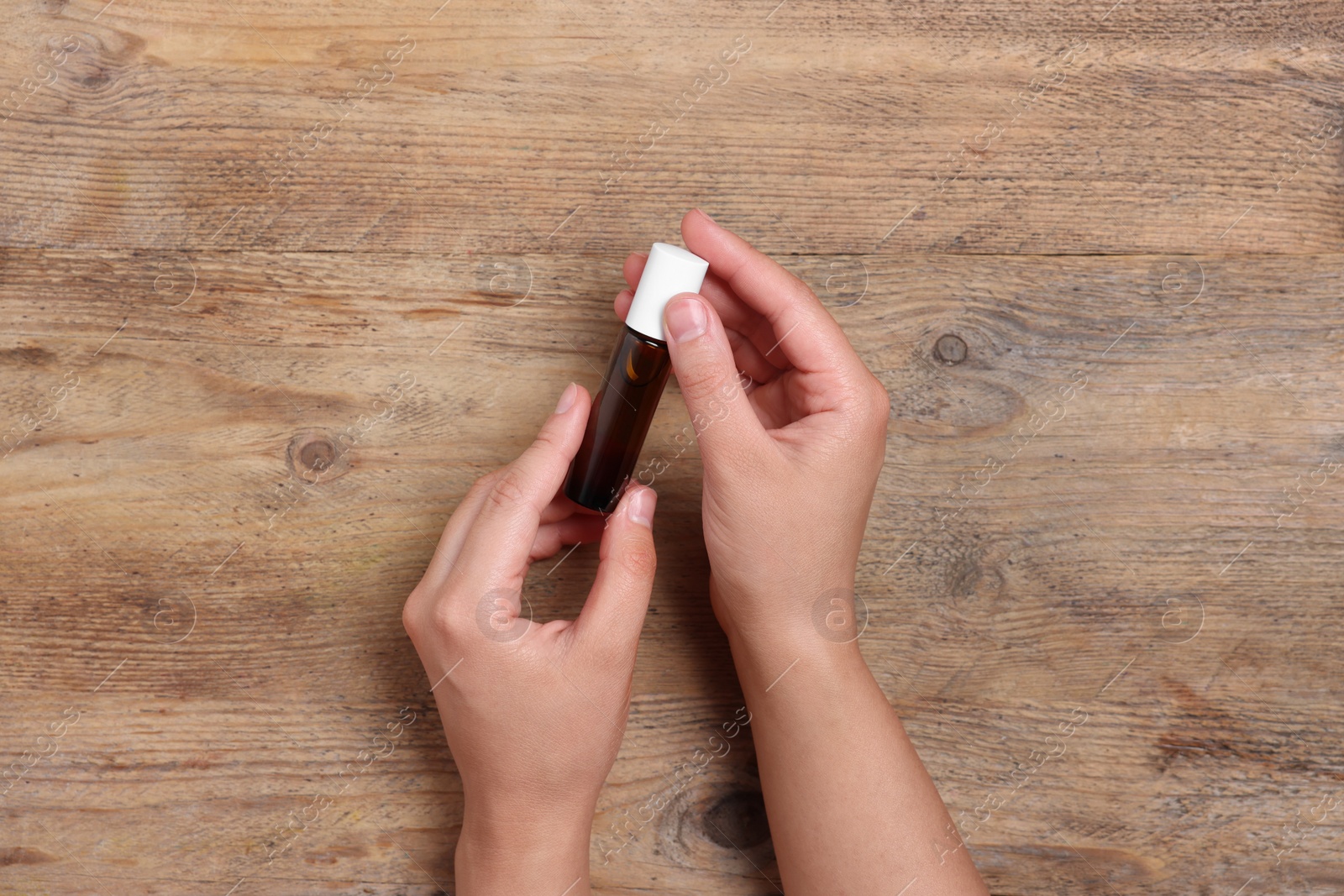 Photo of Woman with bottle of essential oil on wooden background, top view