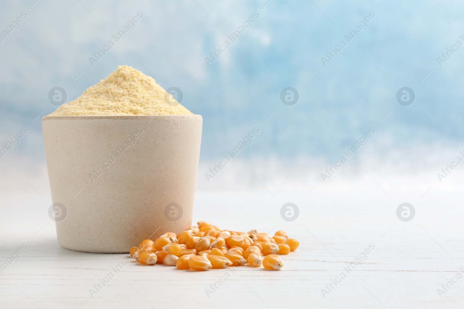 Photo of Bowl with corn flour and kernels on table against color background. Space for text