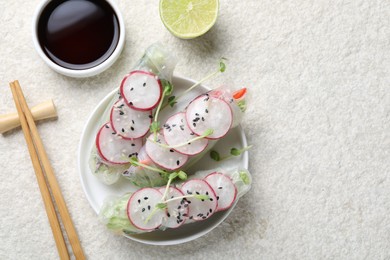 Photo of Delicious spring rolls, chopsticks, soy sauce and lime on light grey table, flat lay. Space for text