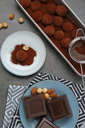 Photo of Delicious chocolate candies powdered with cocoa, sieve and ingredients on grey table, flat lay