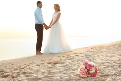 Bouquet and wedding couple on beach. Space for text