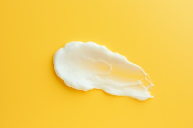 Sample of face cream on yellow background, top view