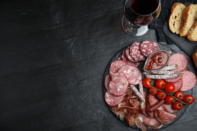 Photo of Different types of sausages with tomatoes served on black table, flat lay. Space for text