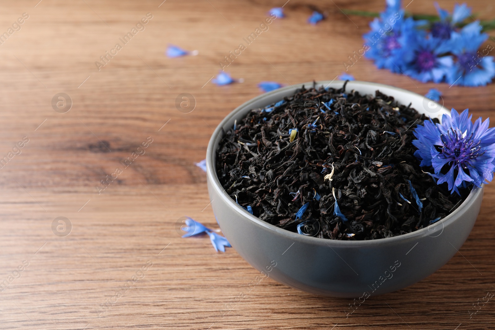 Photo of Dried cornflower tea and fresh flowers on wooden table. Space for text