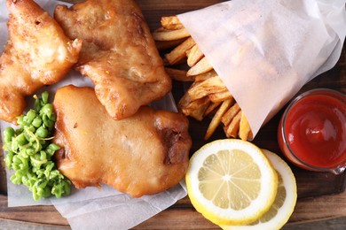 Photo of Tasty fish, chips, sauce and peas on wooden tray, top view