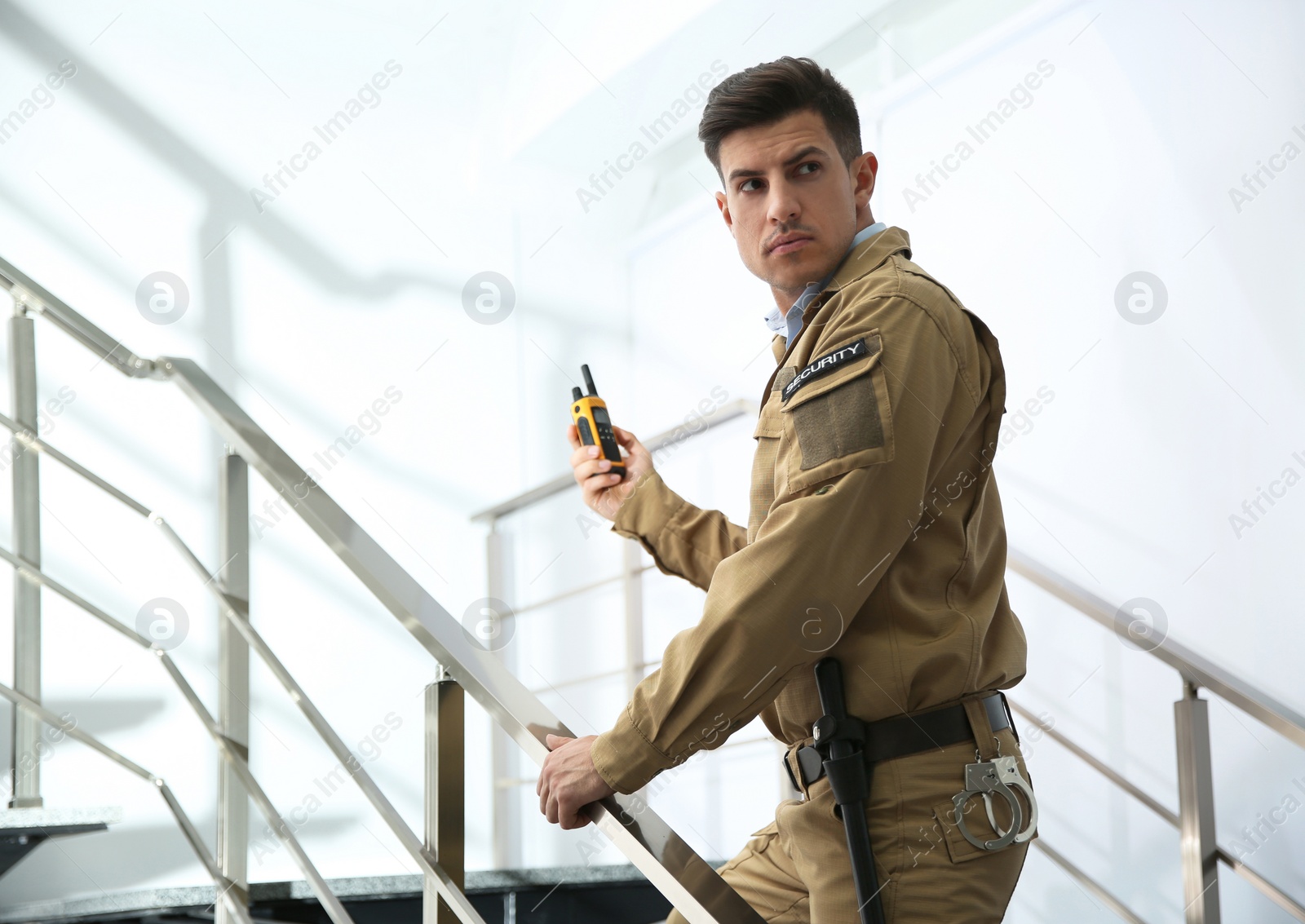 Photo of Professional security guard with portable radio set on stairs indoors