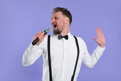 Handsome man with microphone singing on violet background