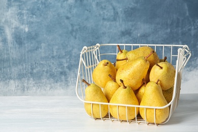 Photo of Basket of fresh ripe pears on table against color background with space for text