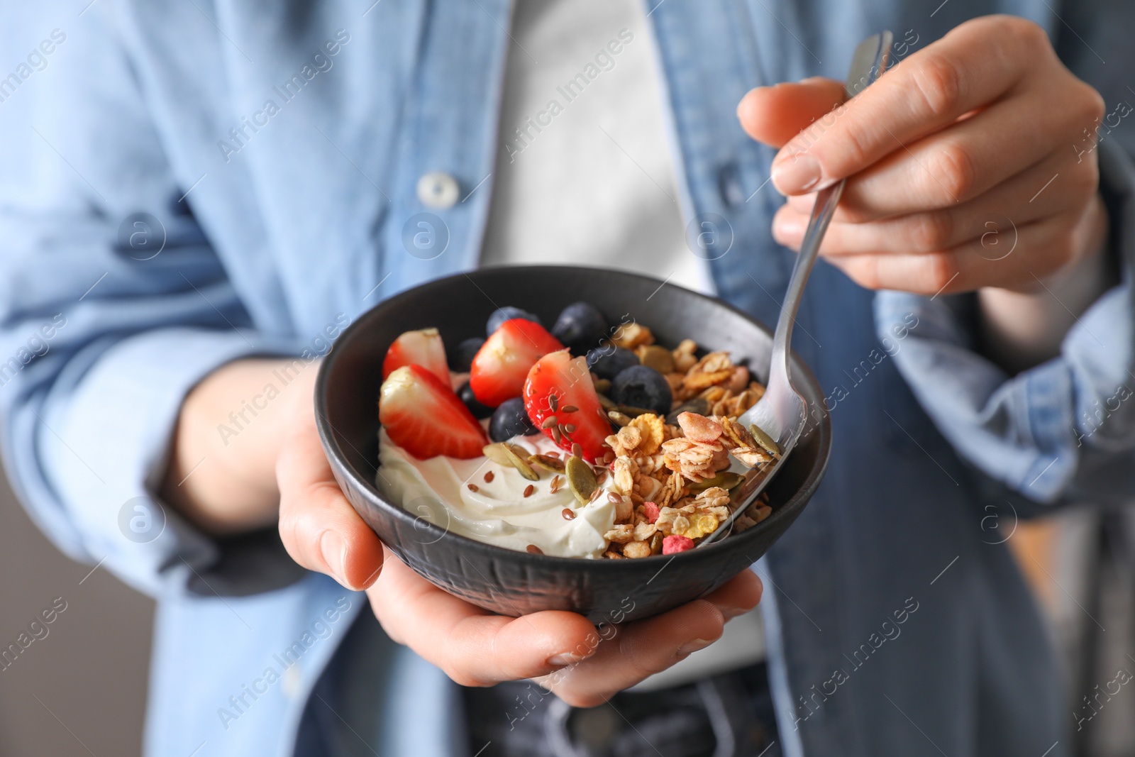 Photo of Woman eating tasty granola with berries, yogurt and seeds, closeup